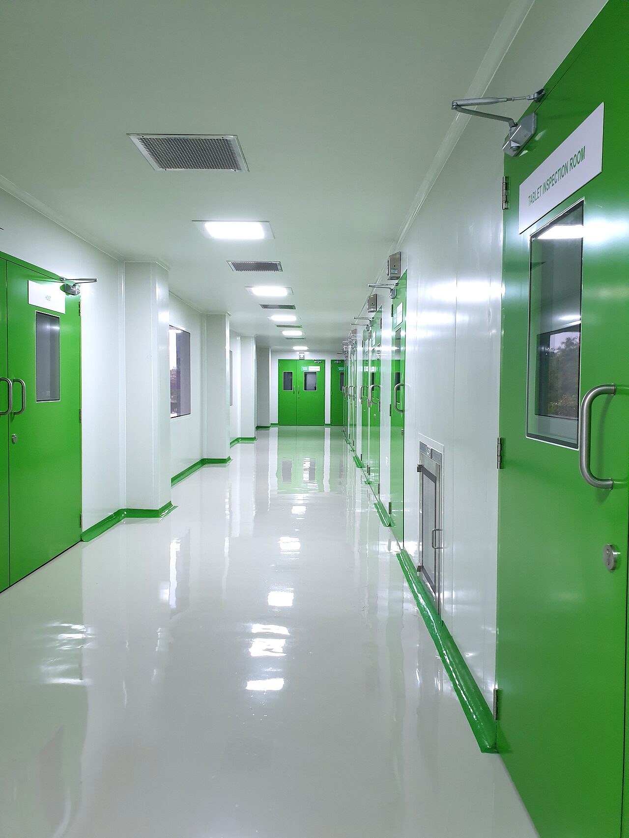 The cleanroom corridor at the Naroda plant: white epoxy flooring and coving, with green airlock doors leading to the tablet inspection room.